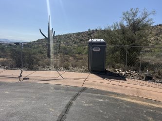 Southwest Sanitation porta potty beside a fence with a saguaro and desert hills behind, Fountain Hills, AZ